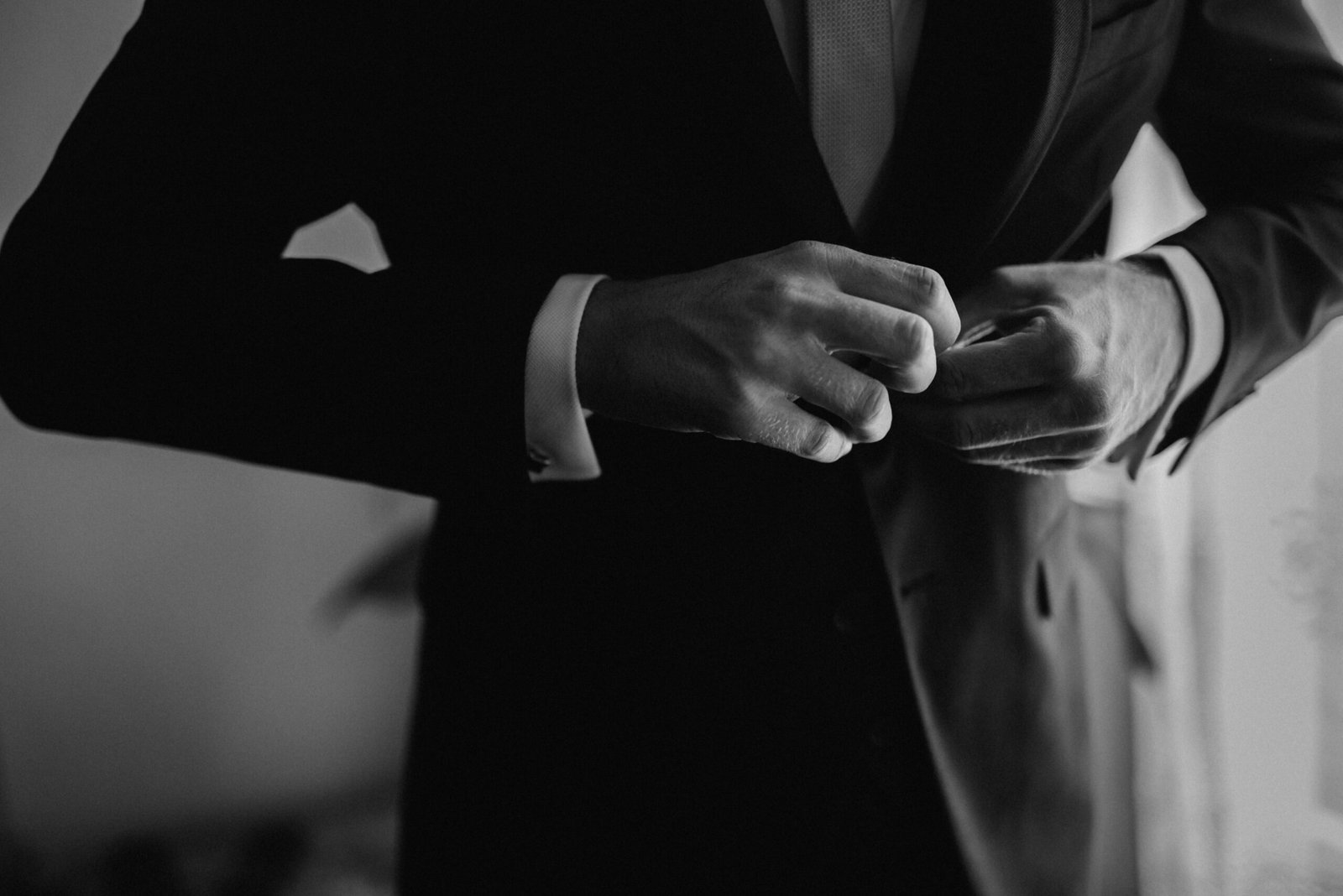 A monochrome close-up of a man adjusting his formal suit jacket, exuding style and class.